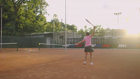 A-tired-brunette-female-tennis-player-walks-along-the-tennis-court-recuperating-and-concentrating.-Break-in-a-tennis-match.-Tennis-player-after-the-match-on-the-map-at-sunset-in-slow-motion.